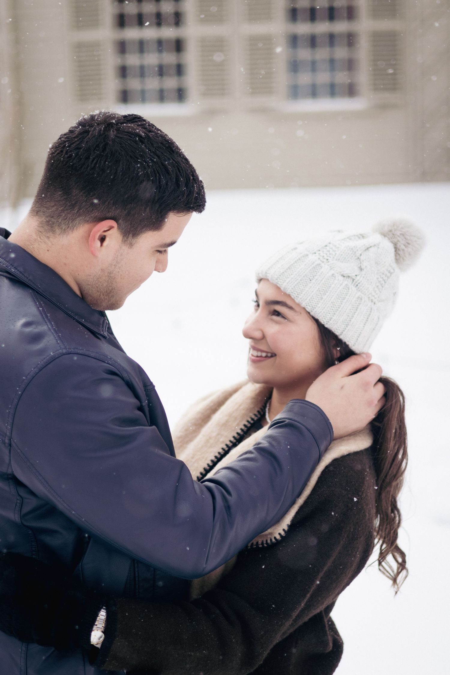 Andover couples photographer capturing a cozy winter portrait of a couple embracing in falling snow during an outdoor session.