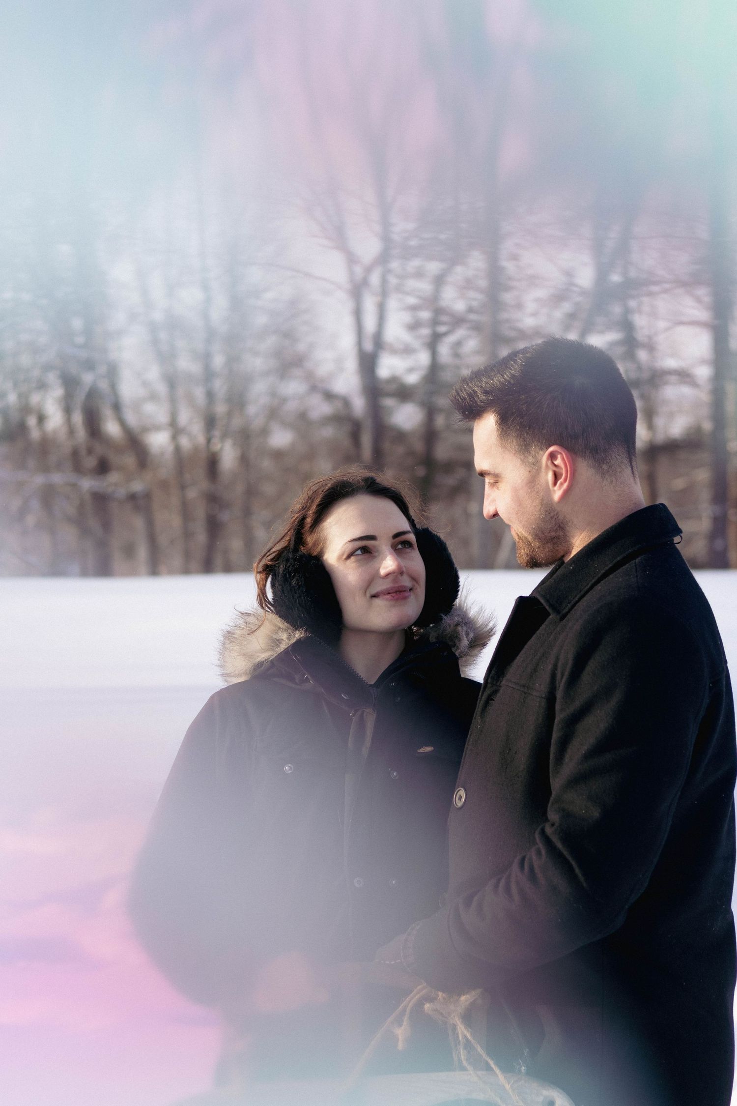 Couple embracing outdoors in falling snow, during a cozy winter portrait session.