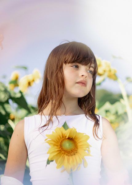 Andover children photographer capturing a natural outdoor portrait of a girl standing in a sunflower field with soft, golden light.