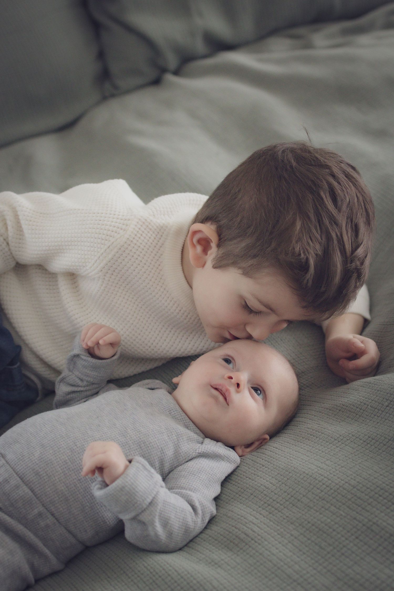 Older sibling lying on a bed and kissing baby brother during a soft, natural family portrait session in Andover, MA.