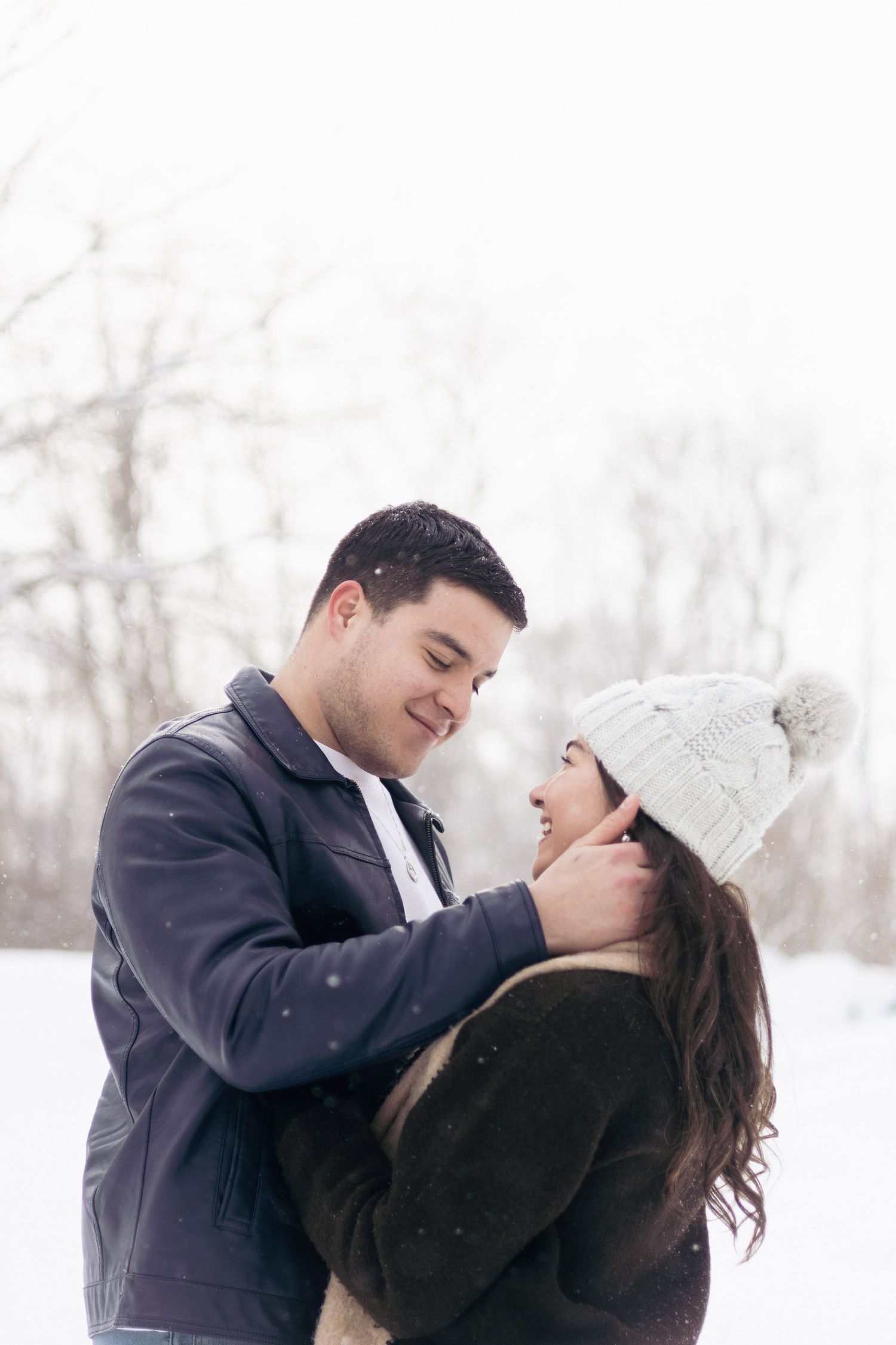 Andover couples photographer capturing a cozy winter portrait of a couple embracing in falling snow during an outdoor session.