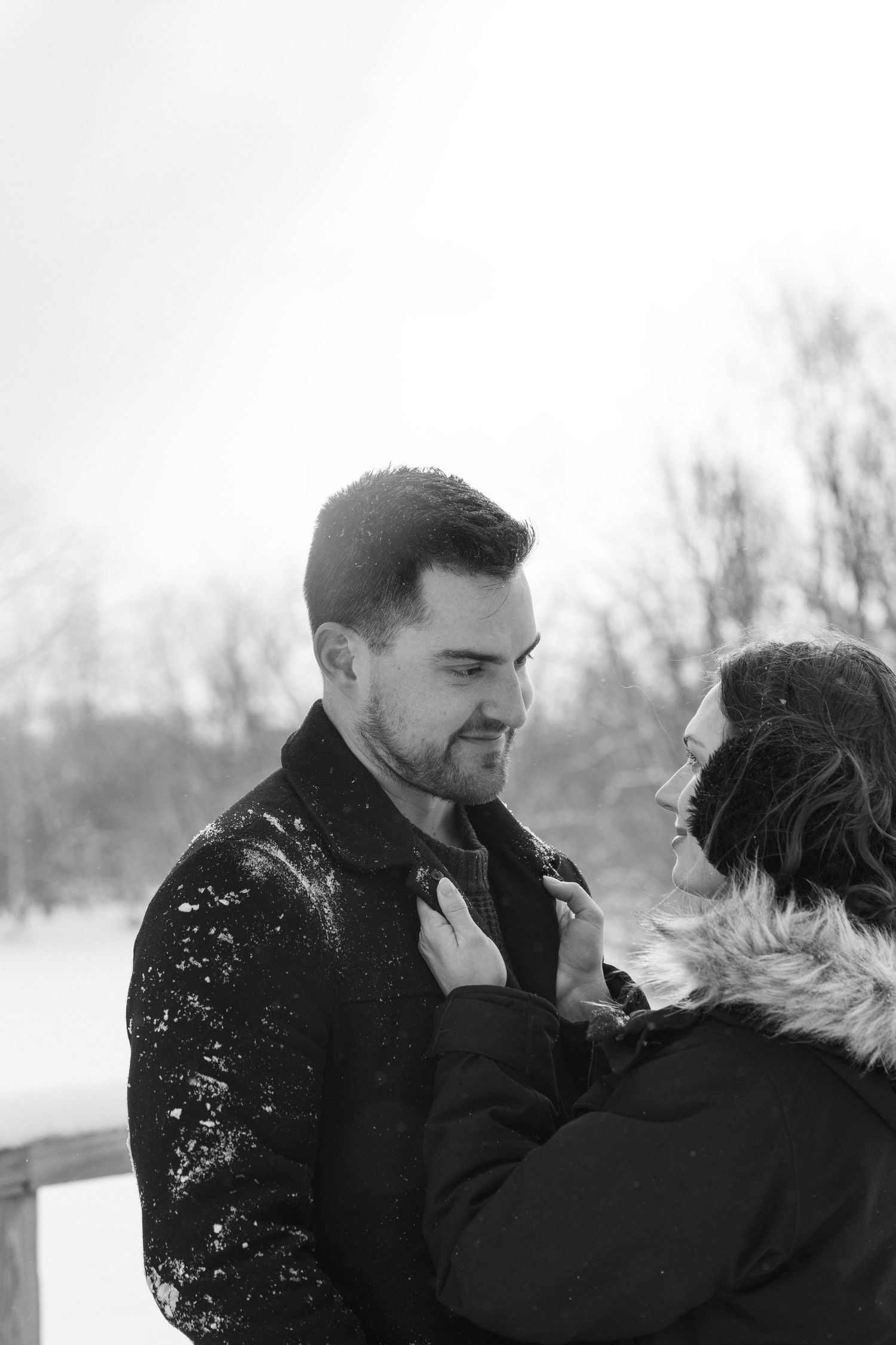 Couple embracing outdoors in falling snow, during a cozy winter portrait session.