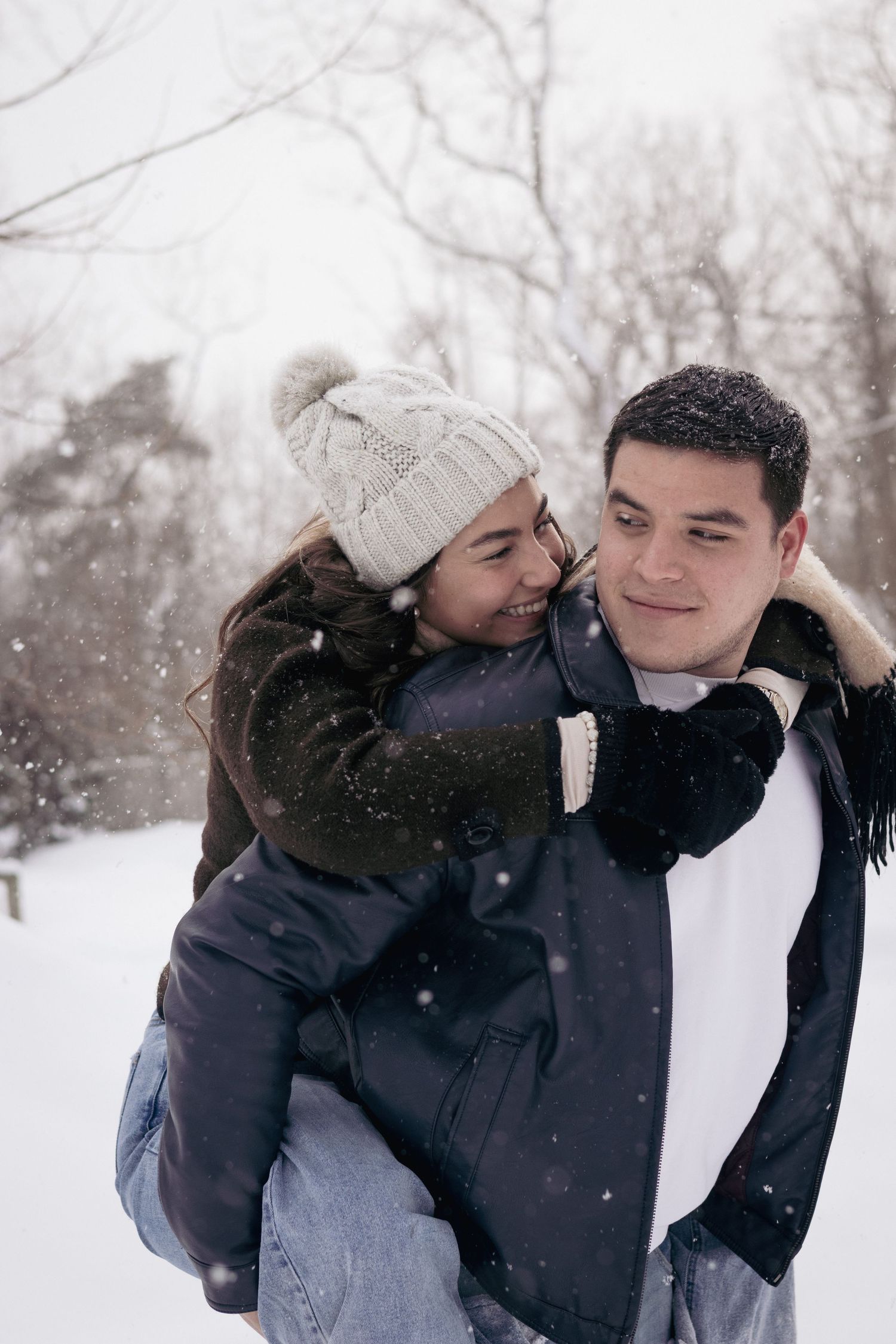 Andover couples photographer capturing a cozy winter portrait of a couple embracing in falling snow during an outdoor session.