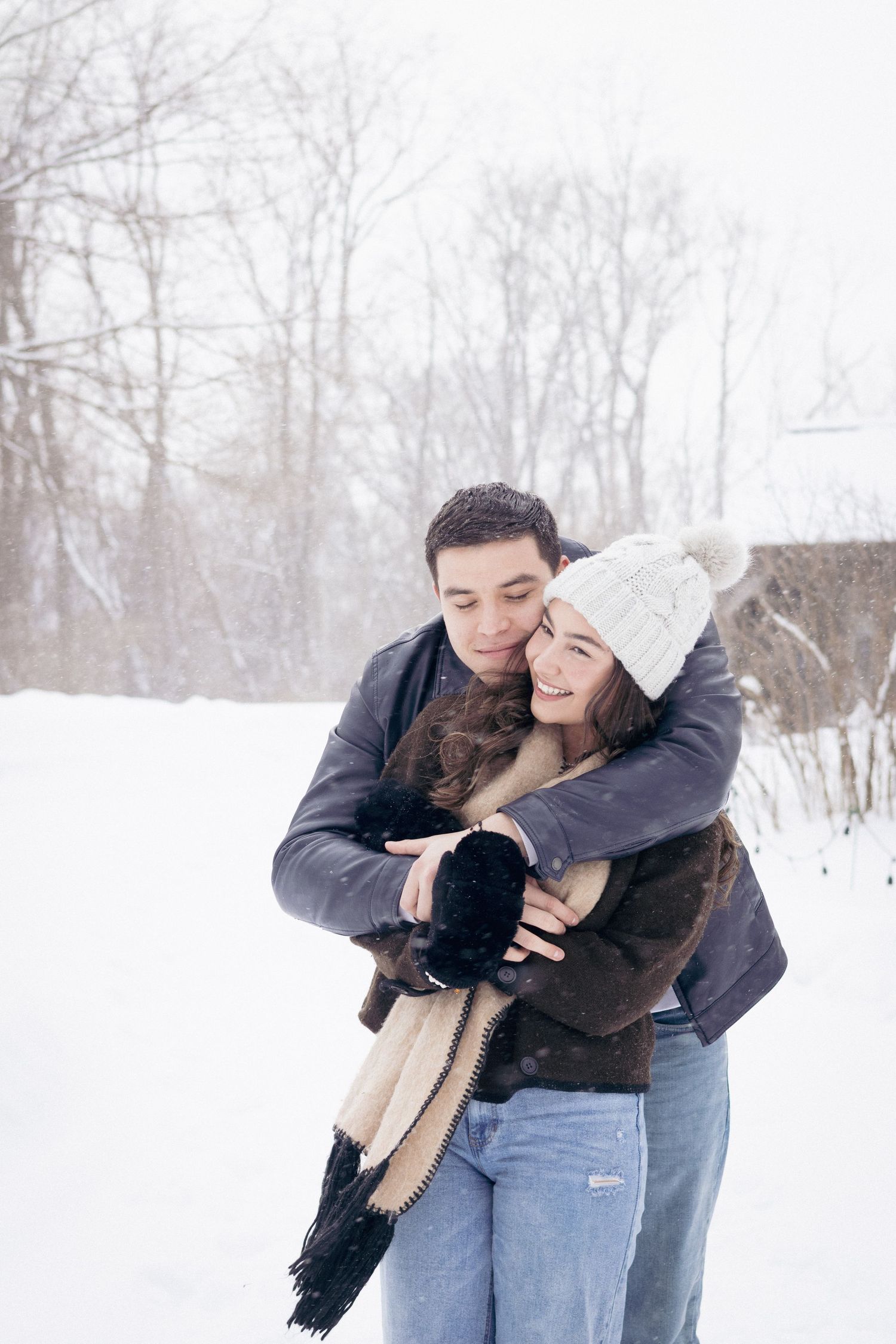 Andover couples photographer capturing a cozy winter portrait of a couple embracing in falling snow during an outdoor session.