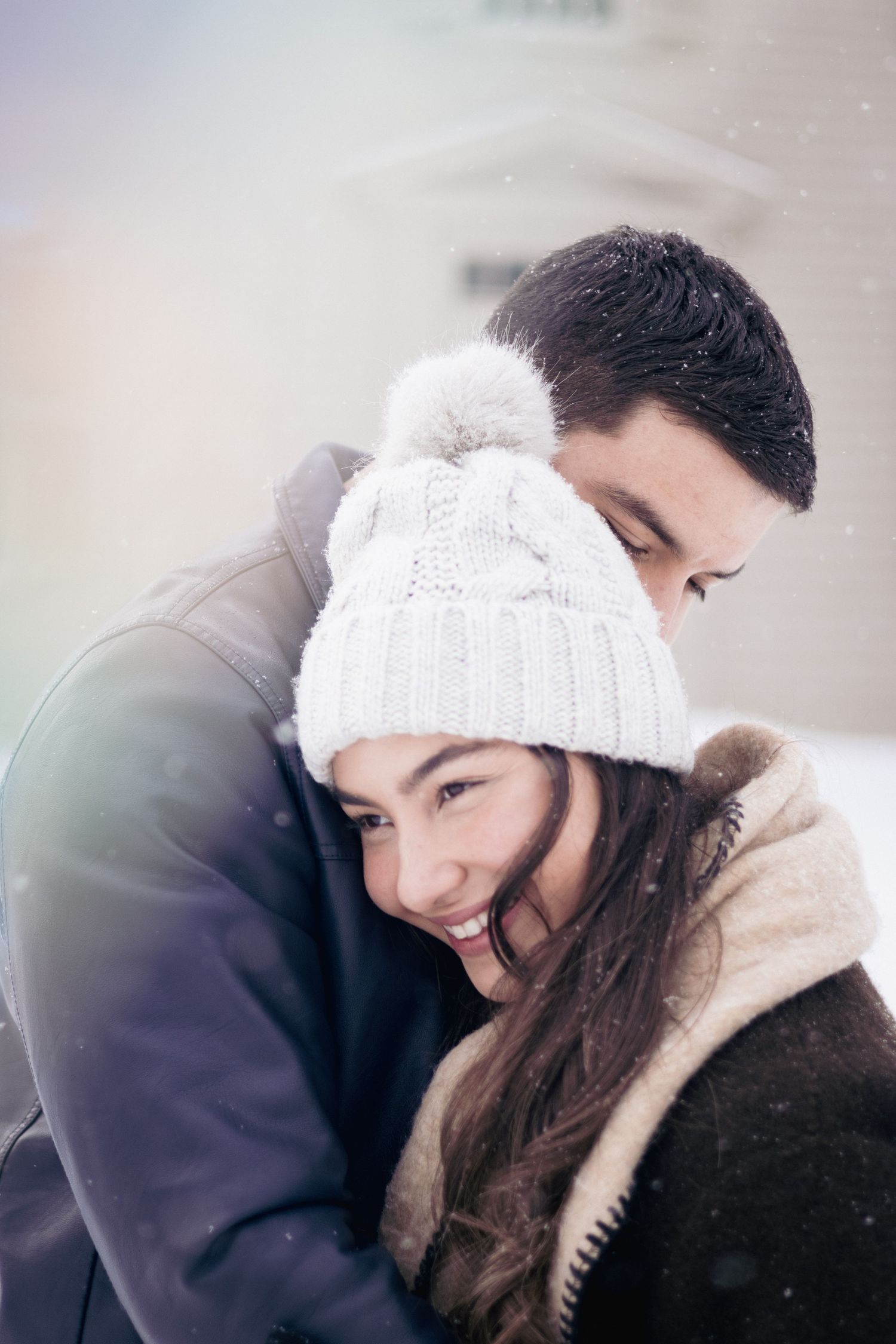 Andover couples photographer capturing a cozy winter portrait of a couple embracing in falling snow during an outdoor session.