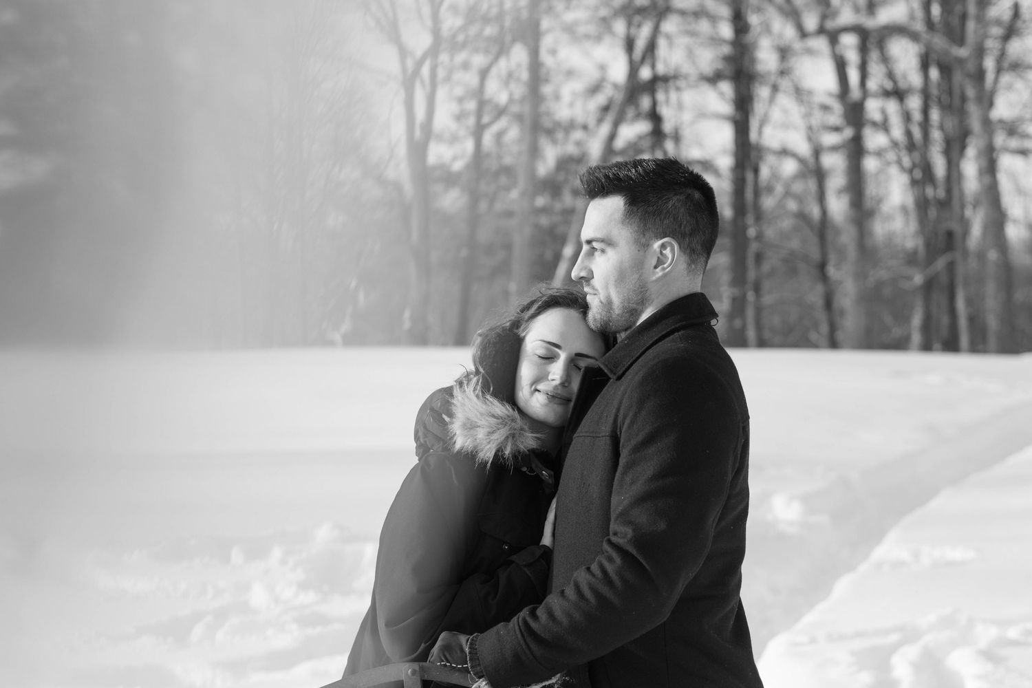 Couple embracing outdoors in falling snow, during a cozy winter portrait session.