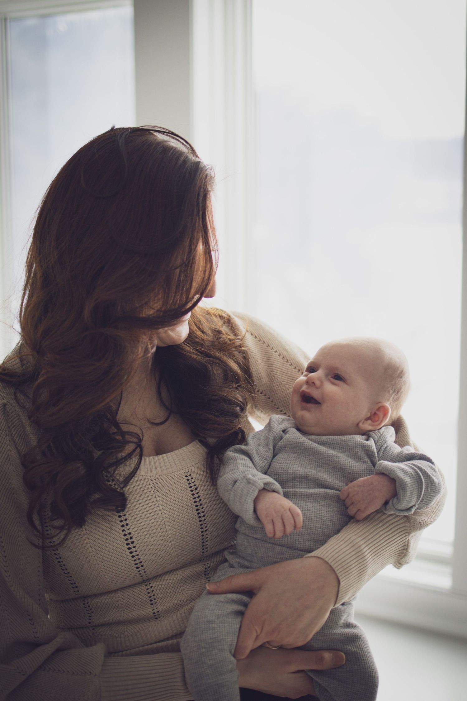 Mother holding her baby while during a soft, natural indoor portrait session with warm, cozy light.
