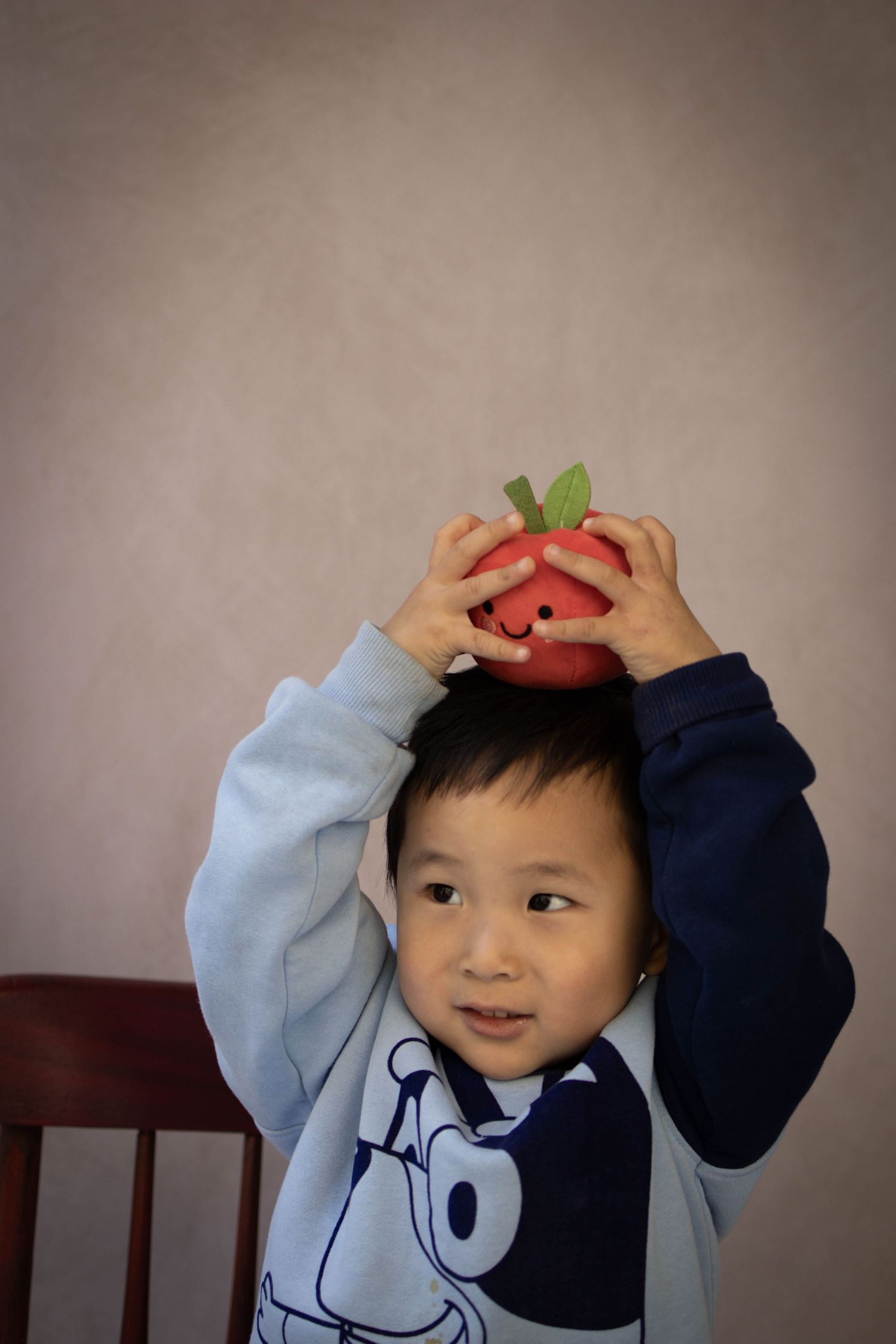 Young child sitting at a desk during a school portrait session, smiling while writing, with school‑themed props including books.