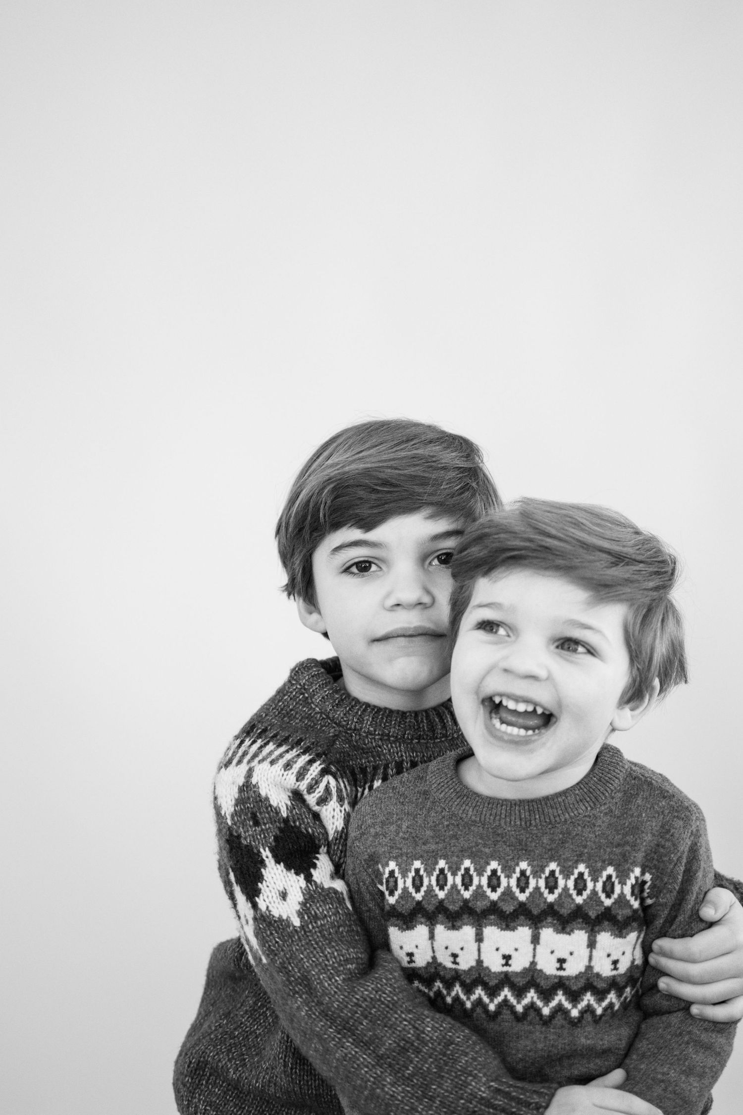 Andover family photographer capturing a black‑and‑white sibling portrait with an older child hugging a younger child in cozy winter sweater.
