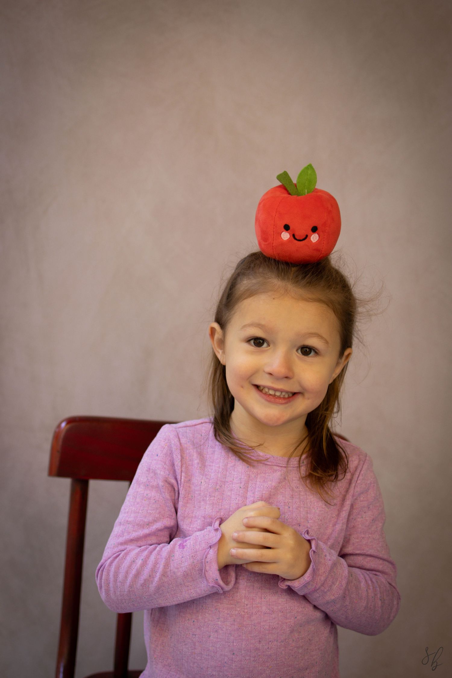 Young child sitting at a desk during a school portrait session, smiling while writing, with school‑themed props including books.