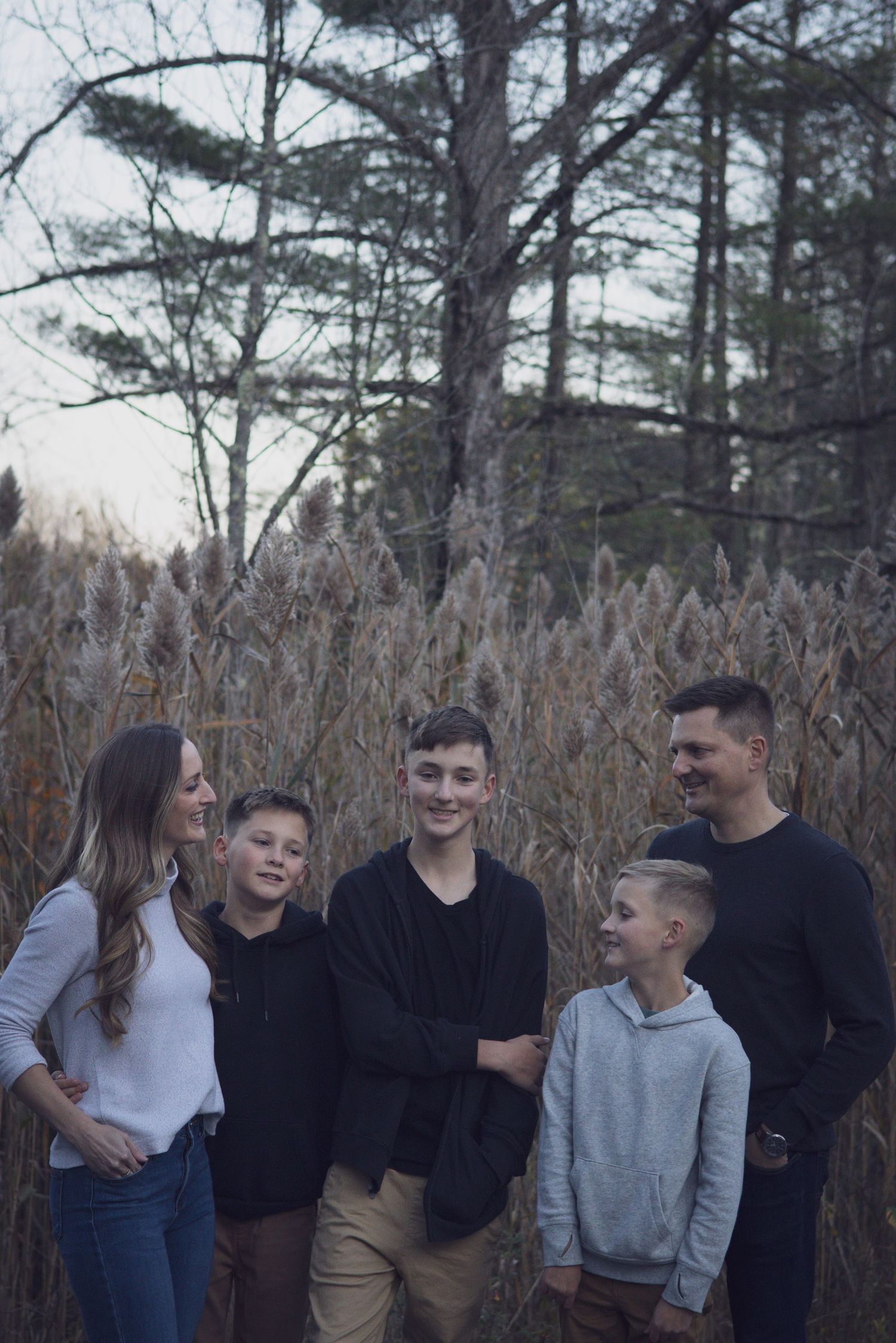 Andover family photographer capturing a fall family portrait of five people standing together in tall grass with autumn foliage.