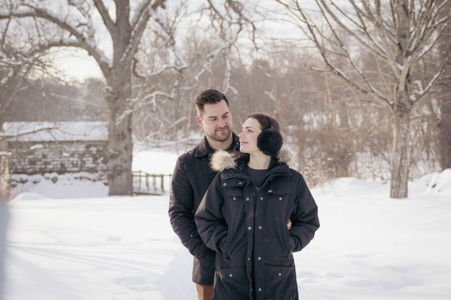 Couple embracing outdoors in falling snow, during a cozy winter portrait session.