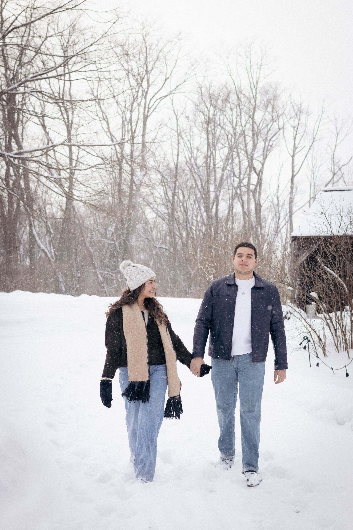 Andover couple photographer capturing a romantic winter session of a couple holding hands and walking through falling snow.