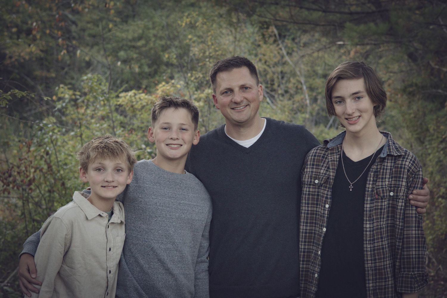 Andover family photographer capturing a fall family portrait of four people standing together in tall grass with autumn foliage.