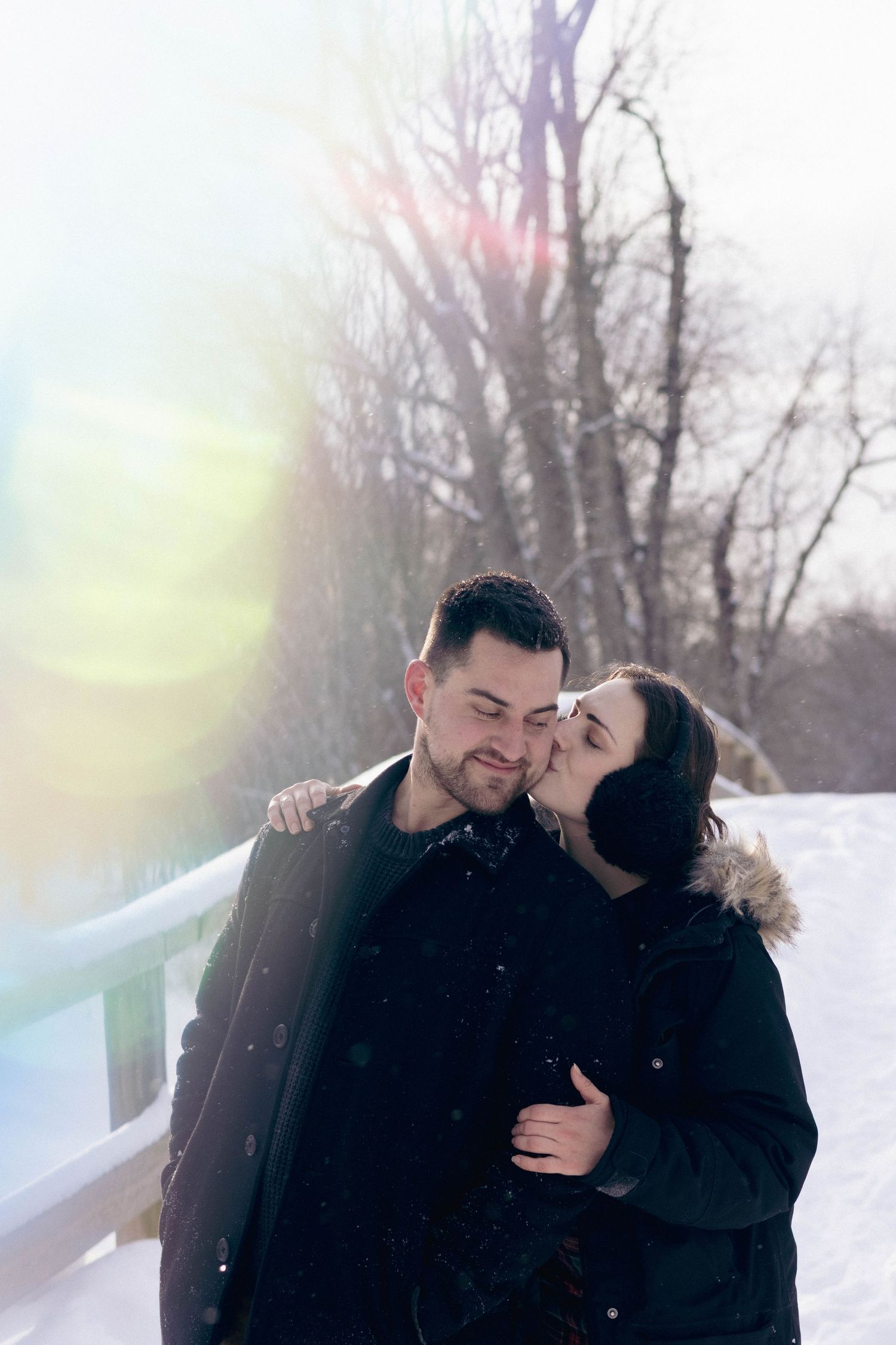Couple embracing outdoors in falling snow, foreheads touching during a cozy winter portrait session.