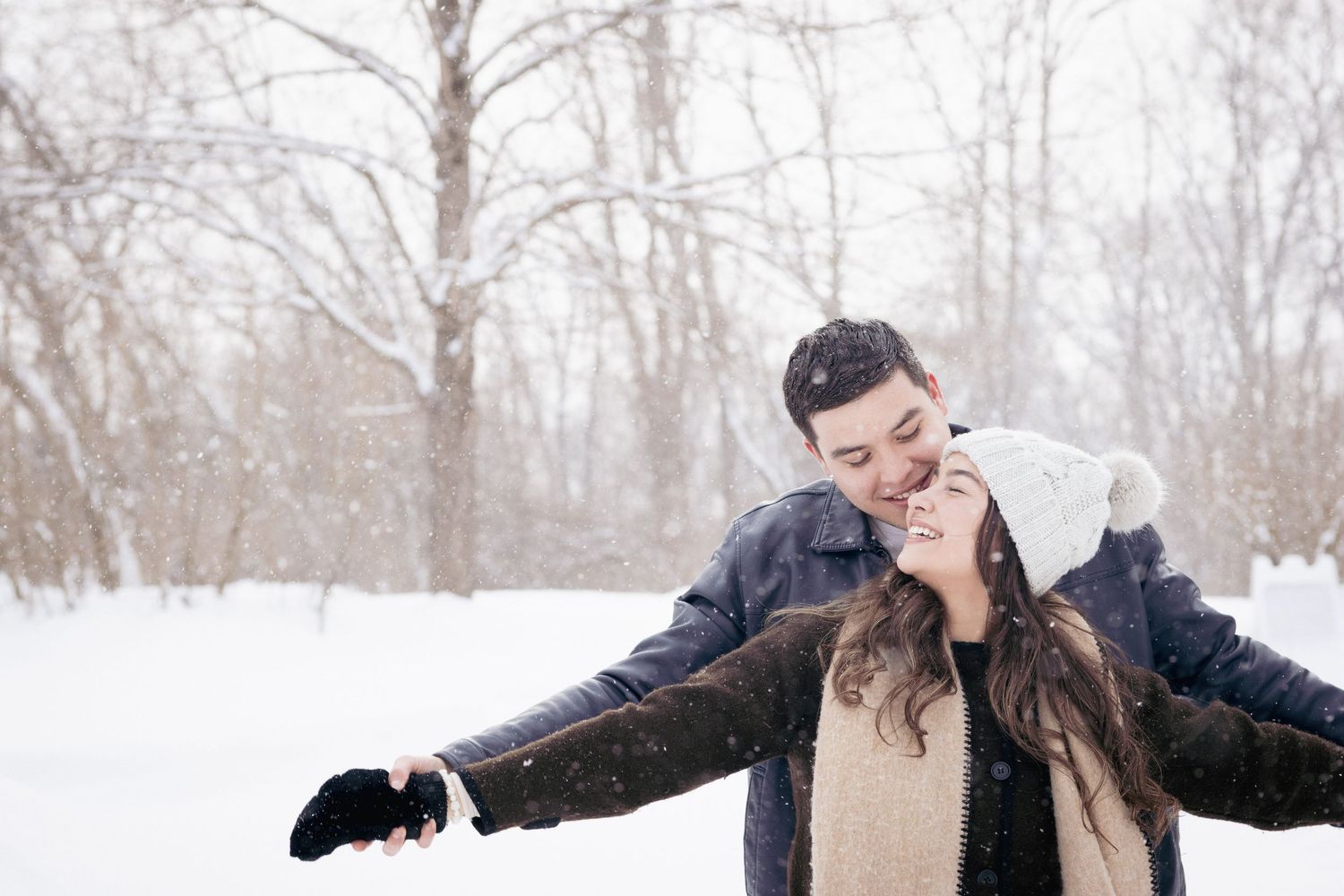 Andover couples photographer capturing a cozy winter portrait of a couple embracing in falling snow during an outdoor session.