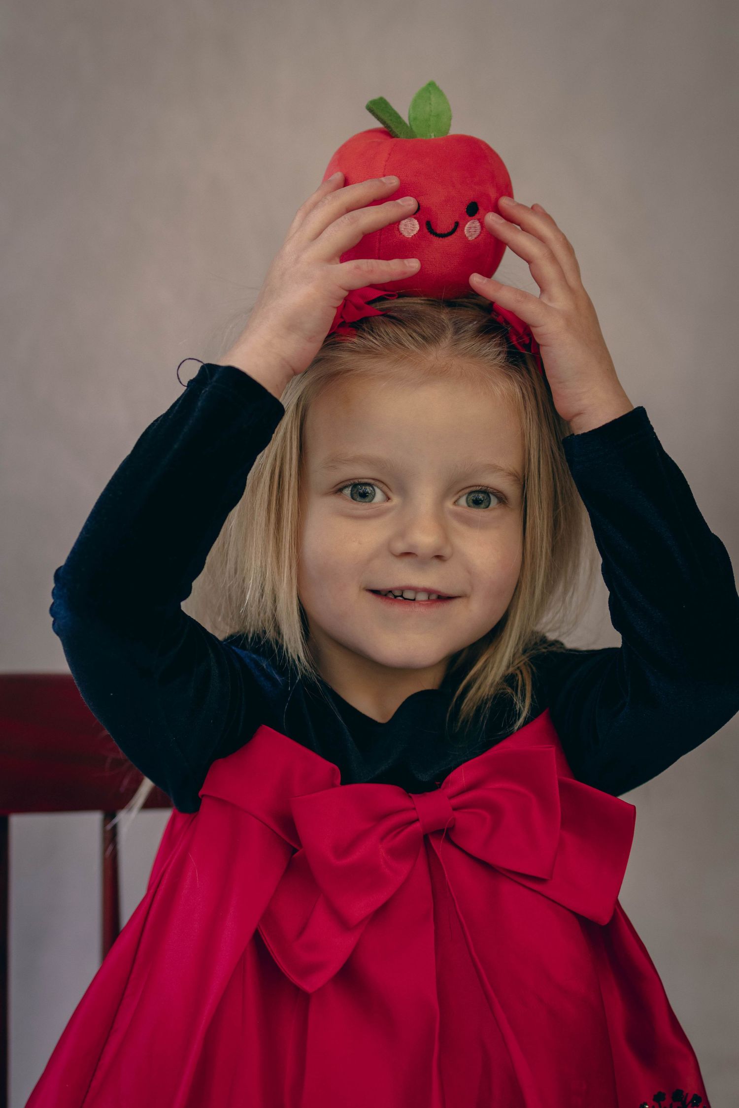 Young child sitting at a desk during a school portrait session, smiling while writing, with school‑themed props including books.