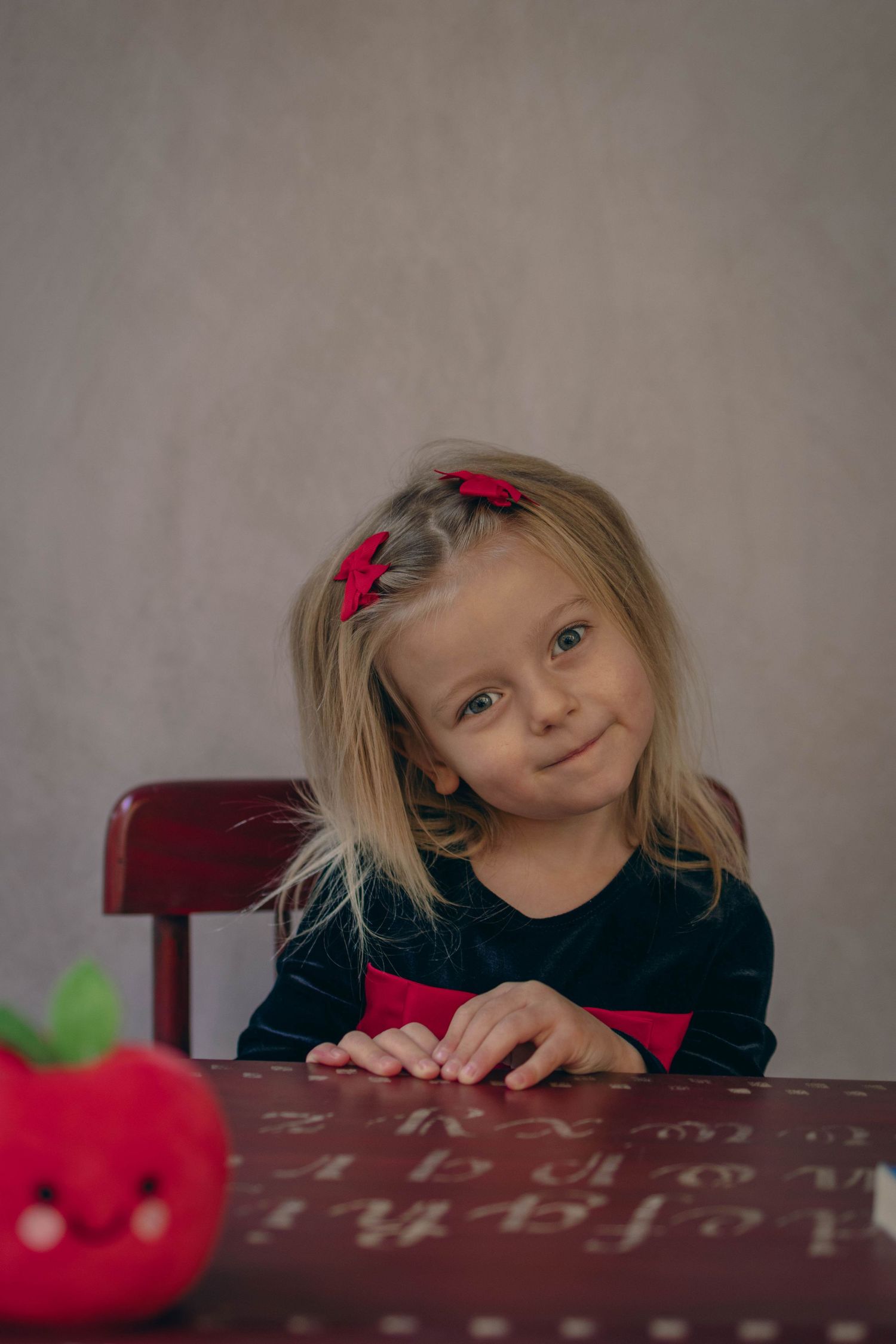 Young child sitting at a desk during a school portrait session, smiling while writing, with school‑themed props including books.