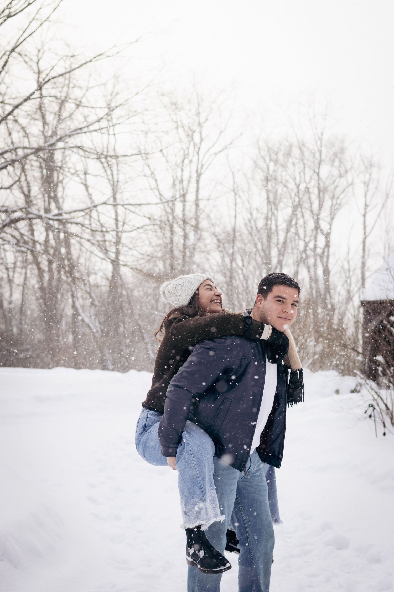Andover couples photographer capturing a cozy winter portrait of a couple embracing in falling snow during an outdoor session.