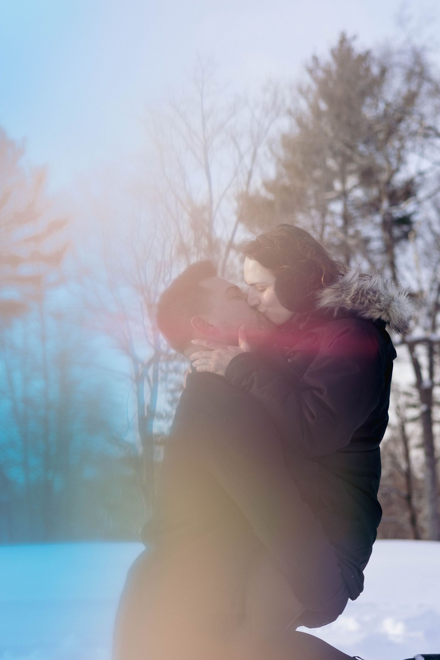 Couple embracing outdoors in falling snow, foreheads touching during a cozy winter portrait session.