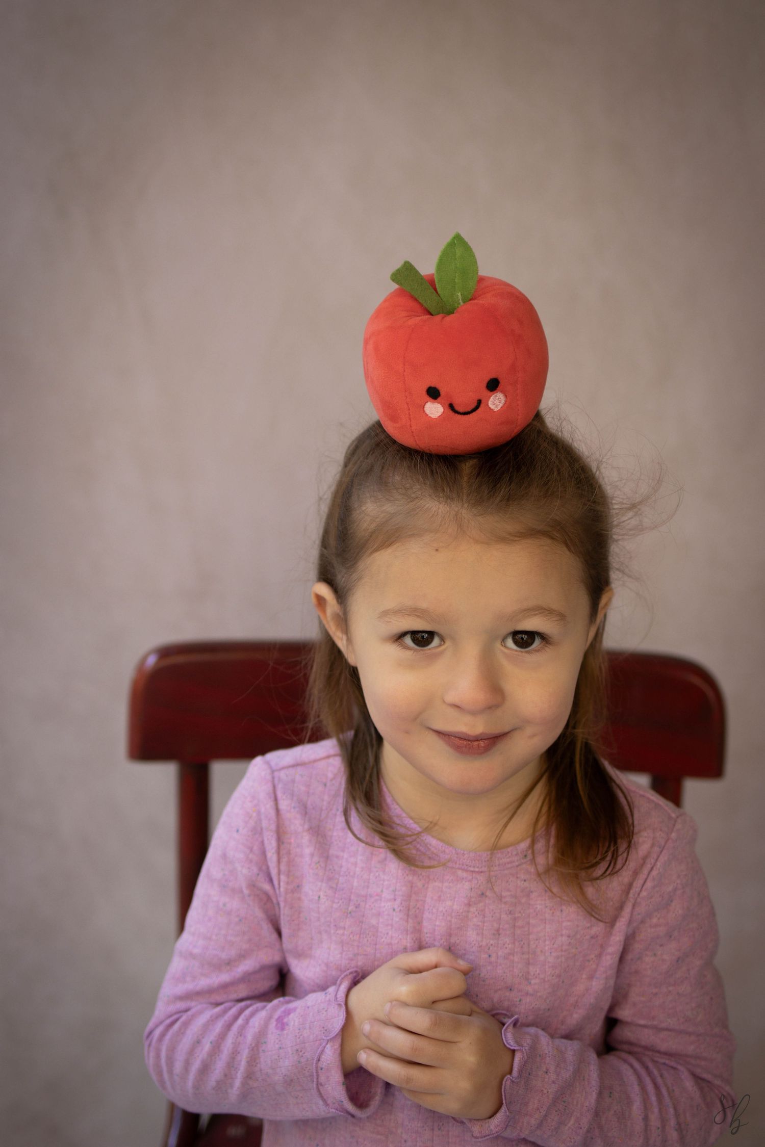 Young child sitting at a desk during a school portrait session, smiling while writing, with school‑themed props including books.