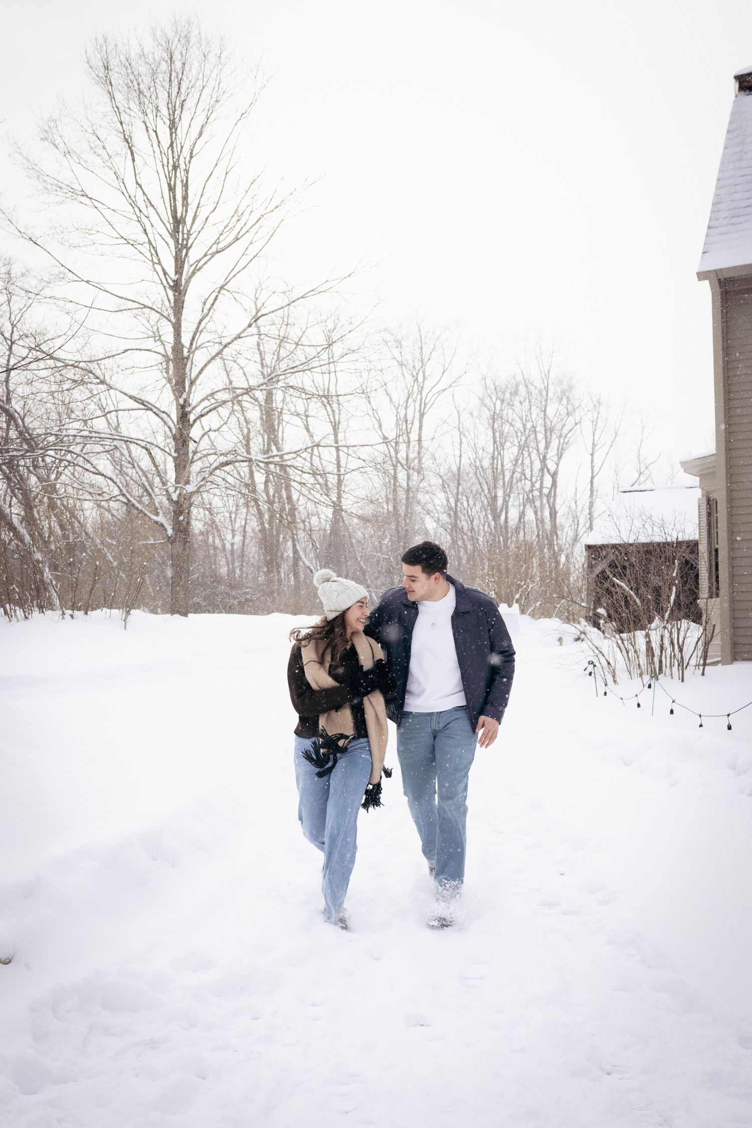 Andover couples photographer capturing a cozy winter portrait of a couple embracing in falling snow during an outdoor session.