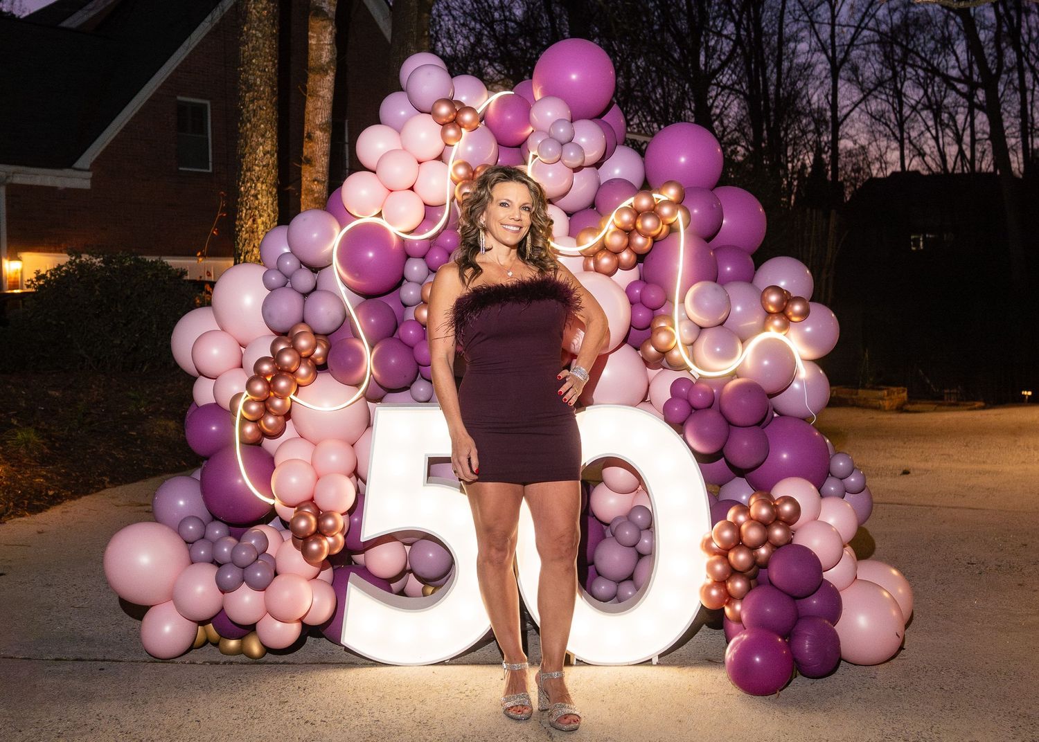Purple balloon arch display with LED lights glowing at night during an outdoor celebration.