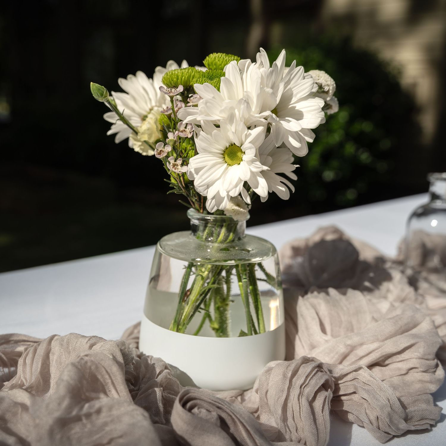 Fresh white daisies arranged in a clear glass vase with soft fabric draping.
