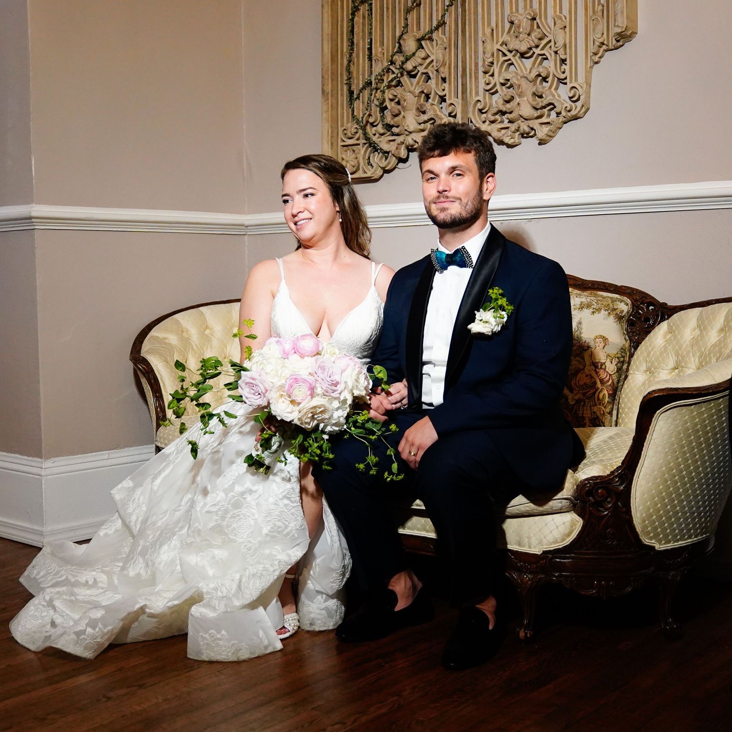 Elegant wedding couple relaxes on vintage furniture in formal indoor setting.