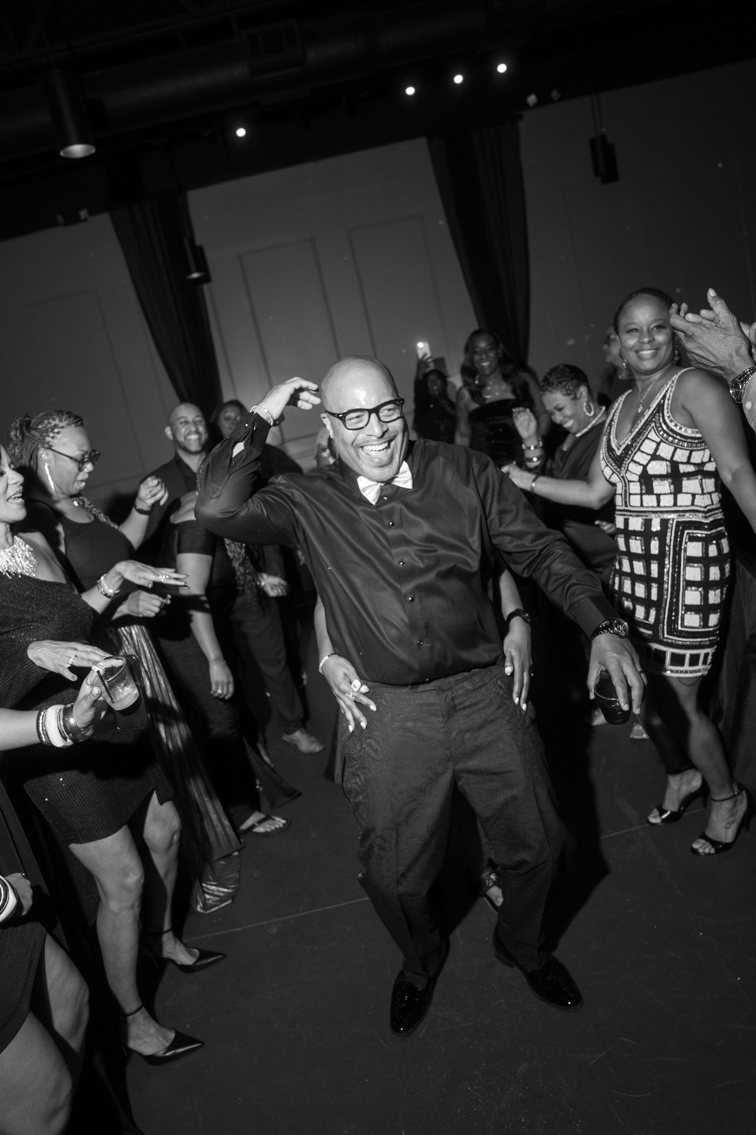 Wedding guests dancing energetically at reception in black and white photography.