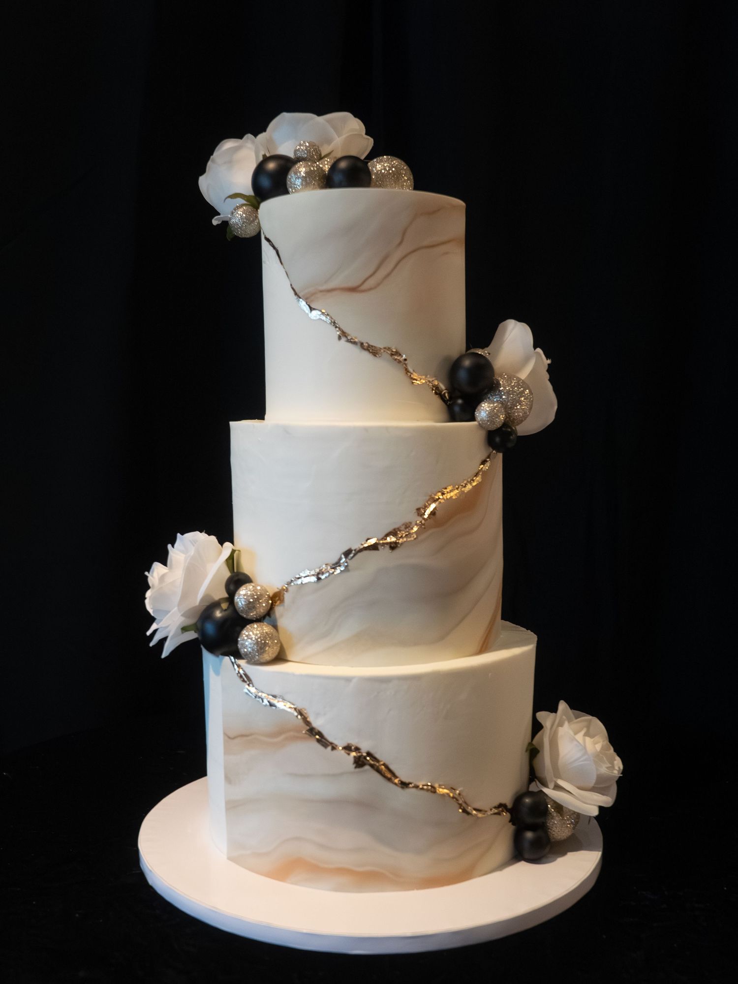Elegant three-tier marble fondant wedding cake with gold veins, black pearls, and white flowers.