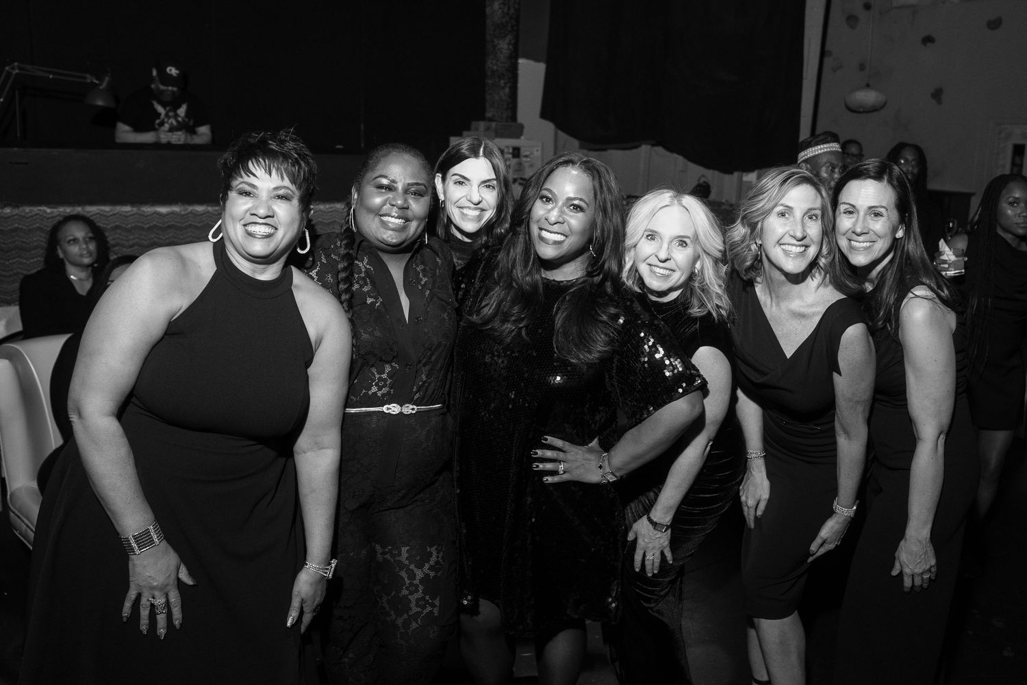 Group of seven women posing together at a formal event, dressed in black attire.