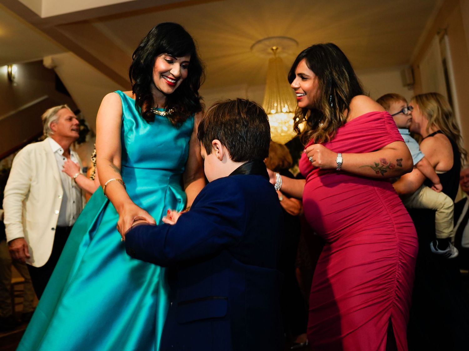 Wedding reception guests dancing in colorful dresses under warm lighting.