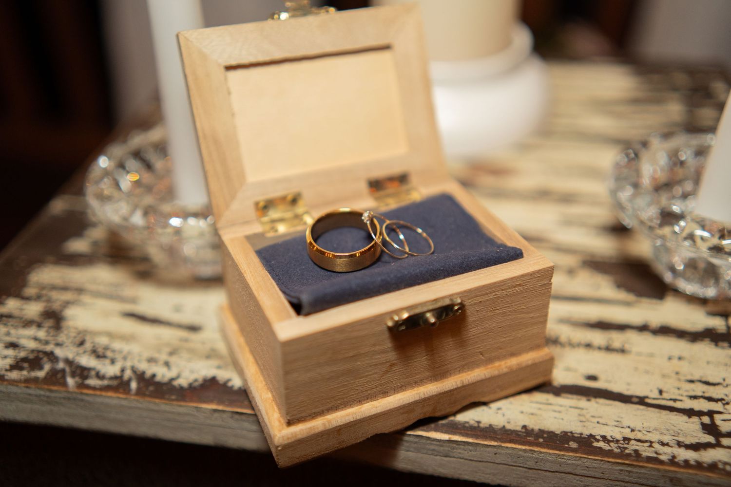 Two gold wedding bands displayed in a small wooden box with blue velvet interior on a rustic table.