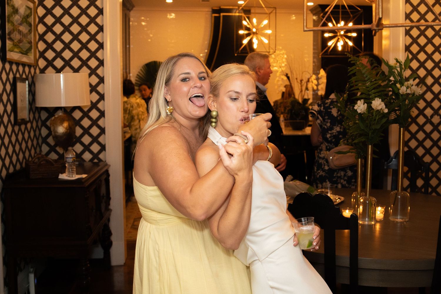 Bridesmaid in yellow dress and bride share a joyful moment dancing together at elegant wedding reception.