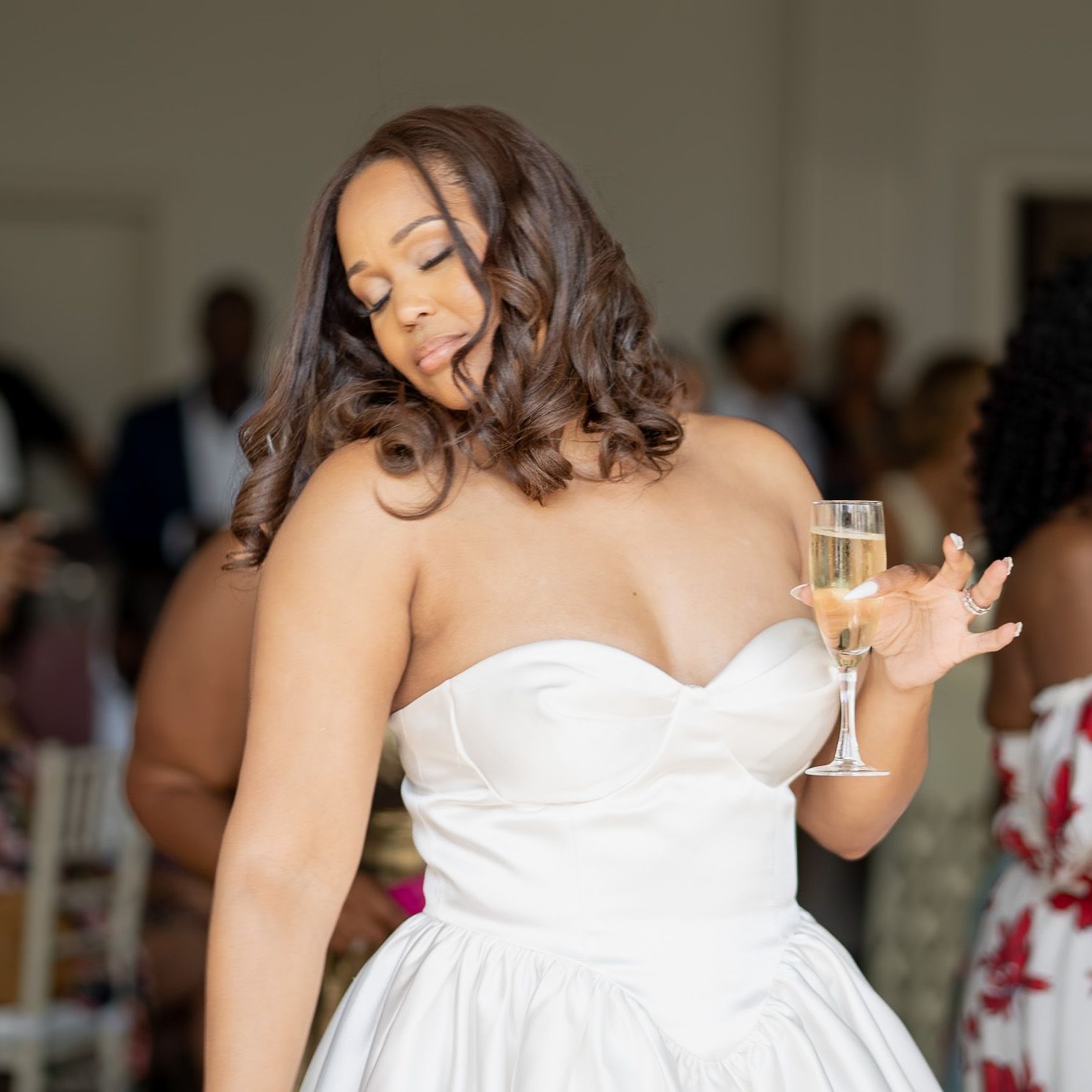Elegant bride in strapless white gown holding champagne glass with joyful expression.