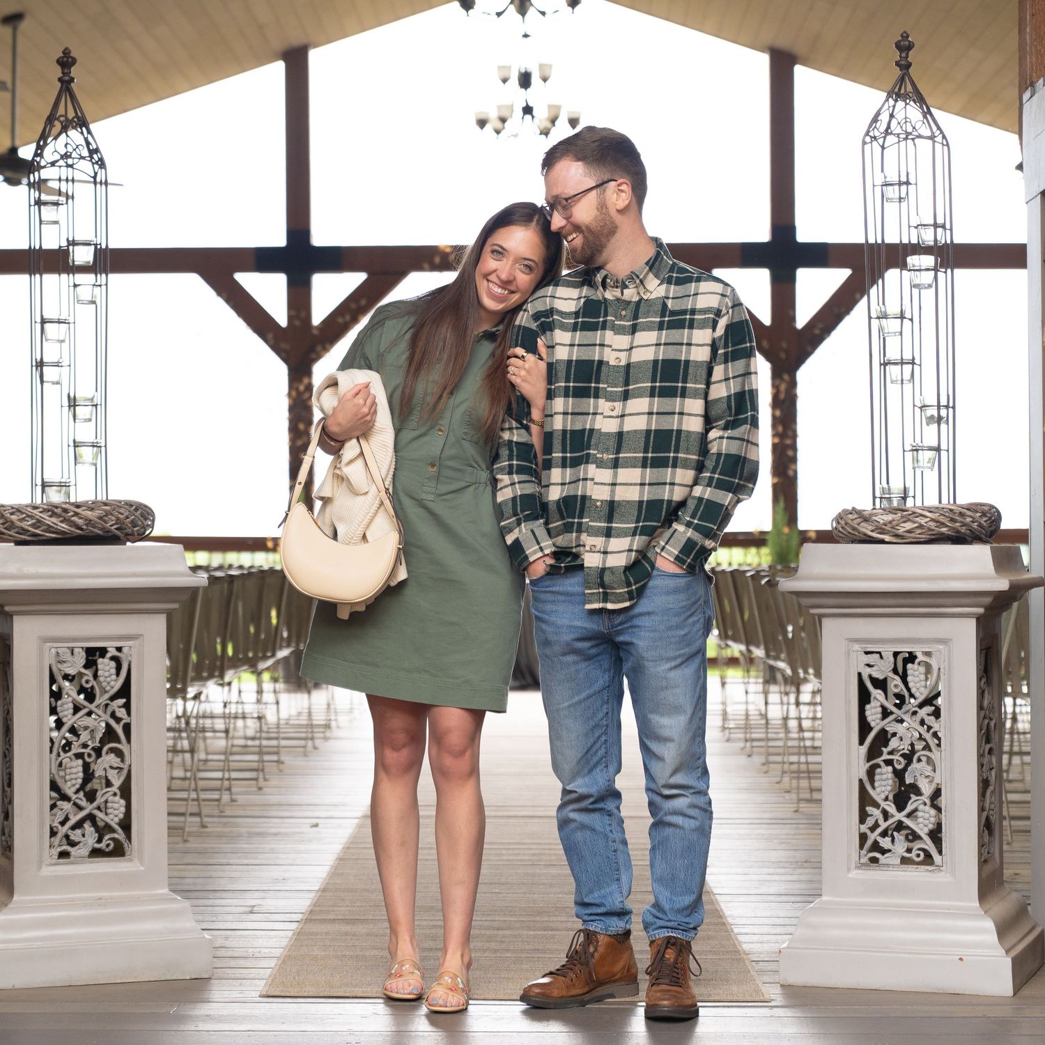 Couple standing together in a rustic indoor venue with decorative chandeliers and wooden beams.