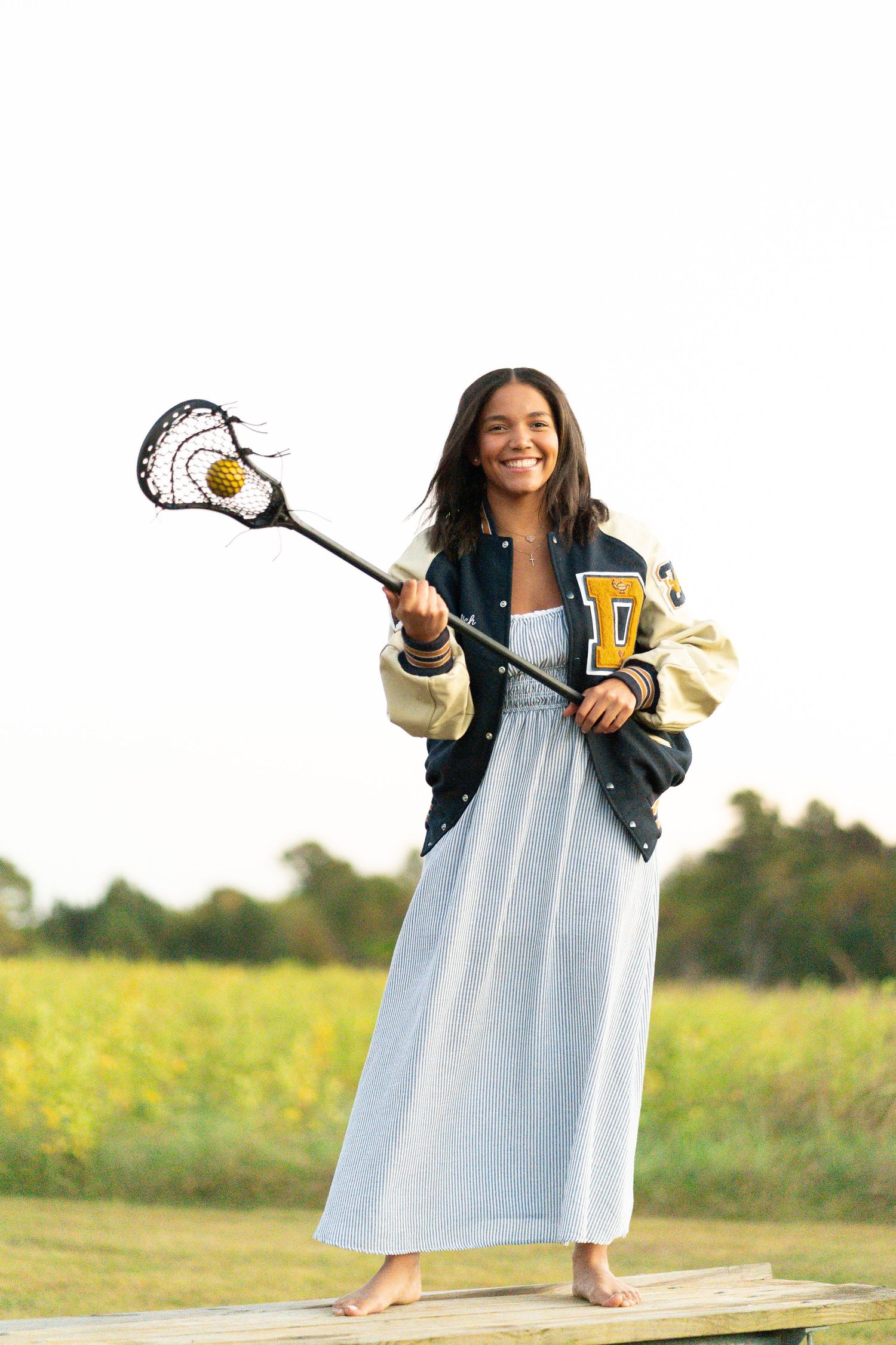 Person in a light blue dress and dark jacket posing playfully in a sunny field.