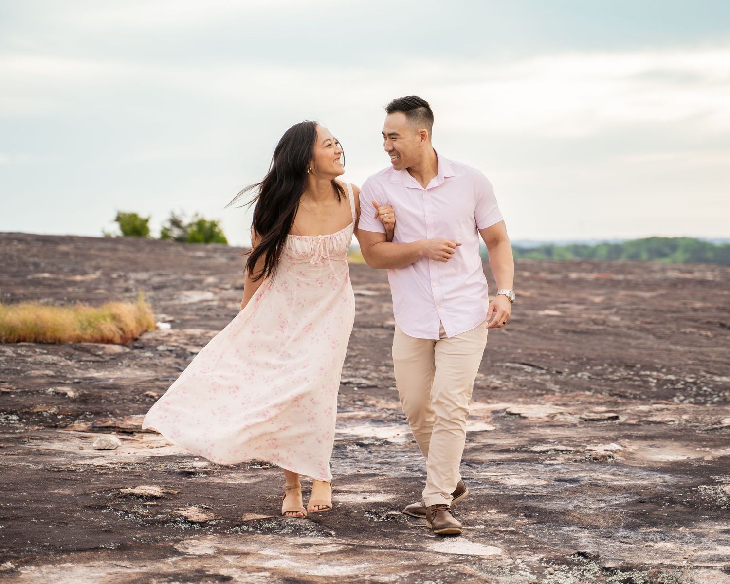 A romantic couple poses together on rocky terrain during a sunset photoshoot.