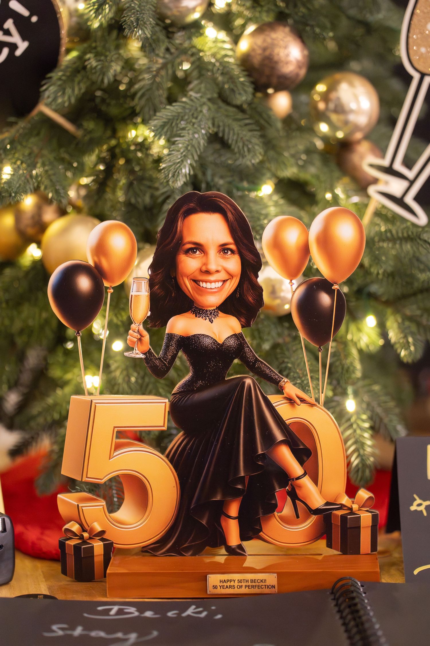 50th birthday caricature figurine of a woman in black dress with gold balloons and champagne.
