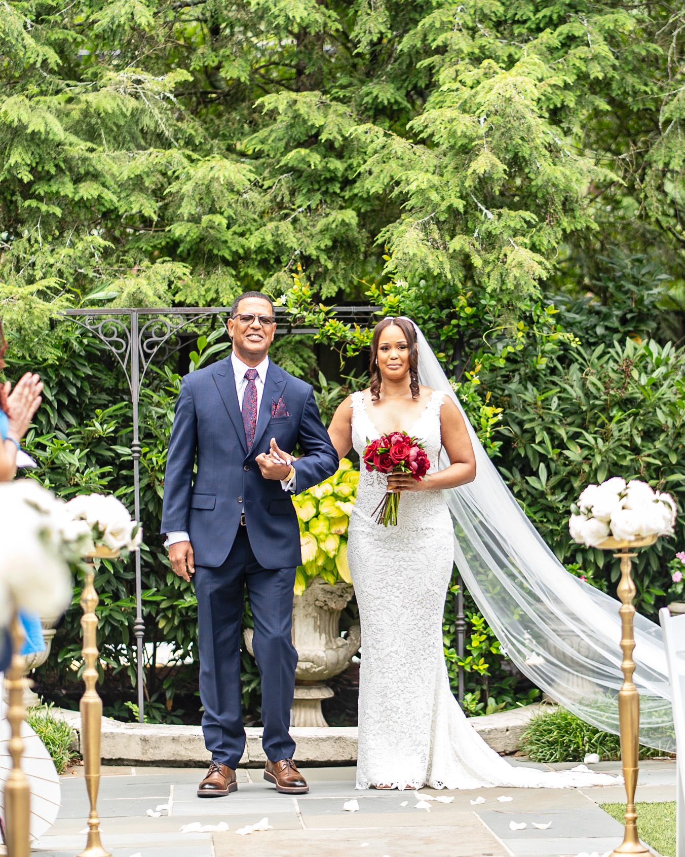 Wedding party poses for photos on garden path with elegant decor and greenery.
