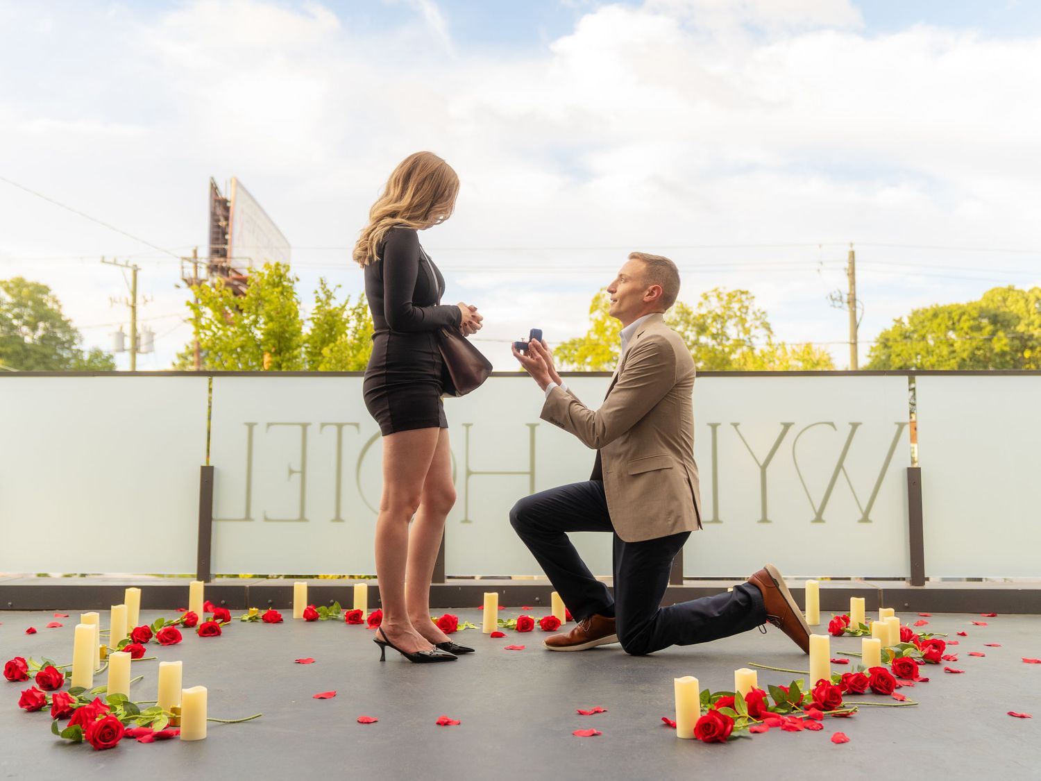 A rooftop proposal setup with red rose petals and candles arranged in a romantic pattern.