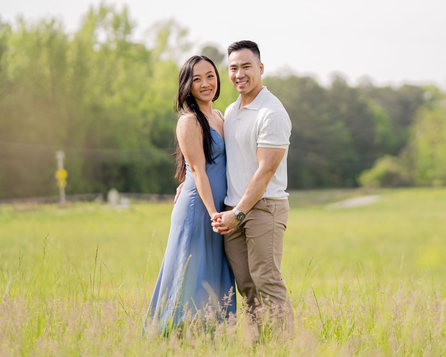 Couple sharing intimate moment in sunny field with rustic barn backdrop.
