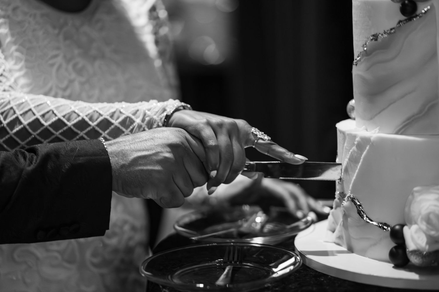 Bride and groom cutting wedding cake together in elegant black and white photo.