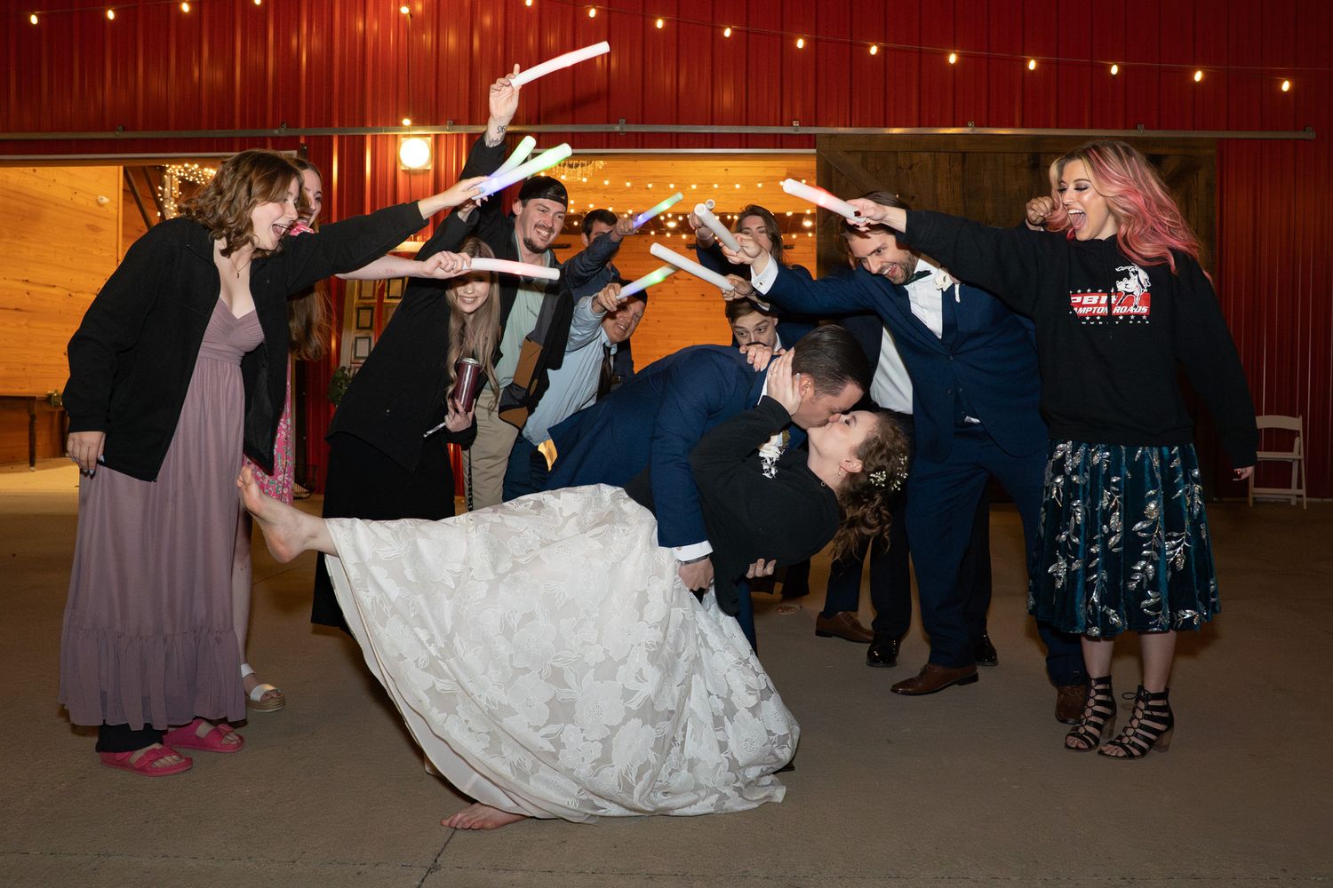 Bride and groom dip kiss under arch of raised items held by wedding guests on dance floor at reception.