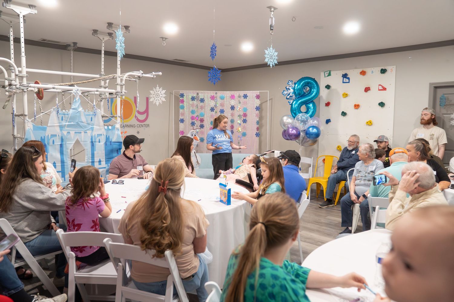 Children and adults gather at a Frozen-themed birthday party with balloon decorations and a castle centerpiece.