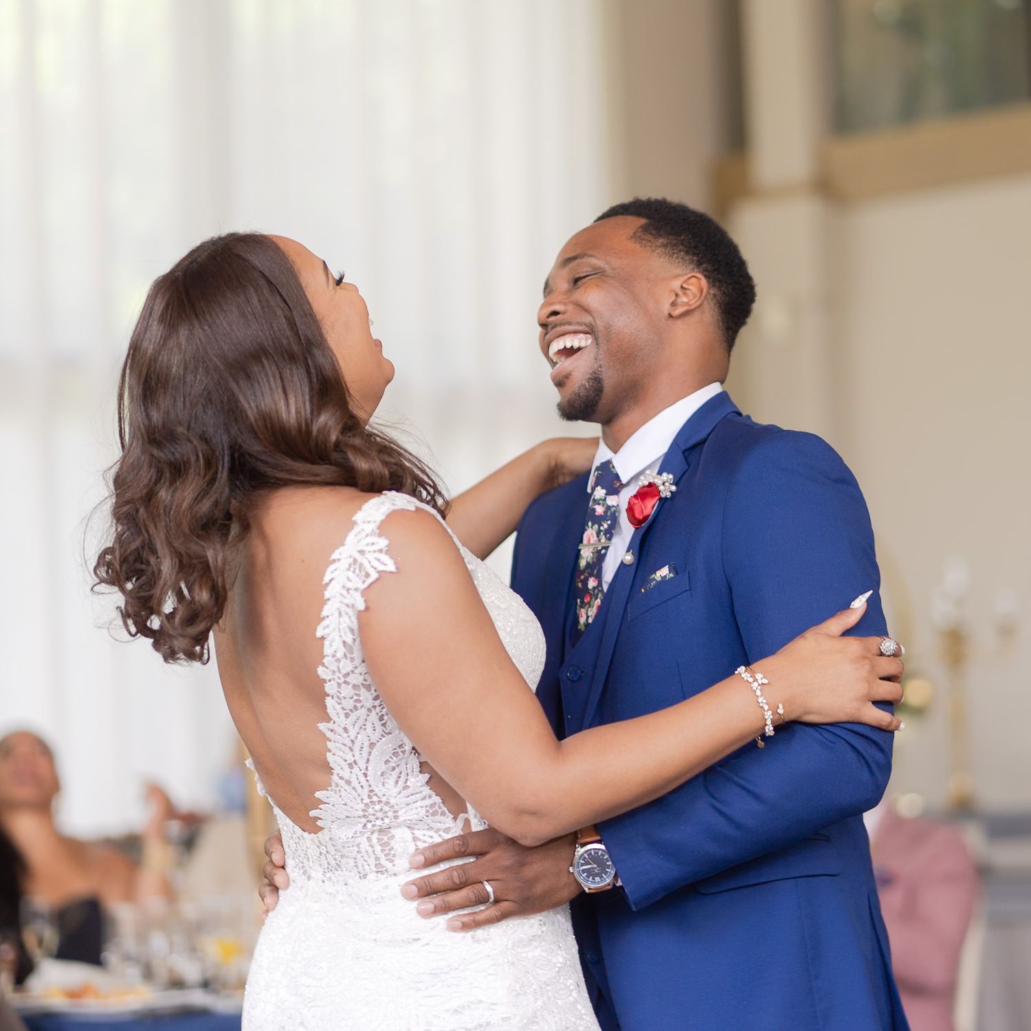 A joyful couple shares their first dance at a wedding, bride in lace gown and groom in blue suit.