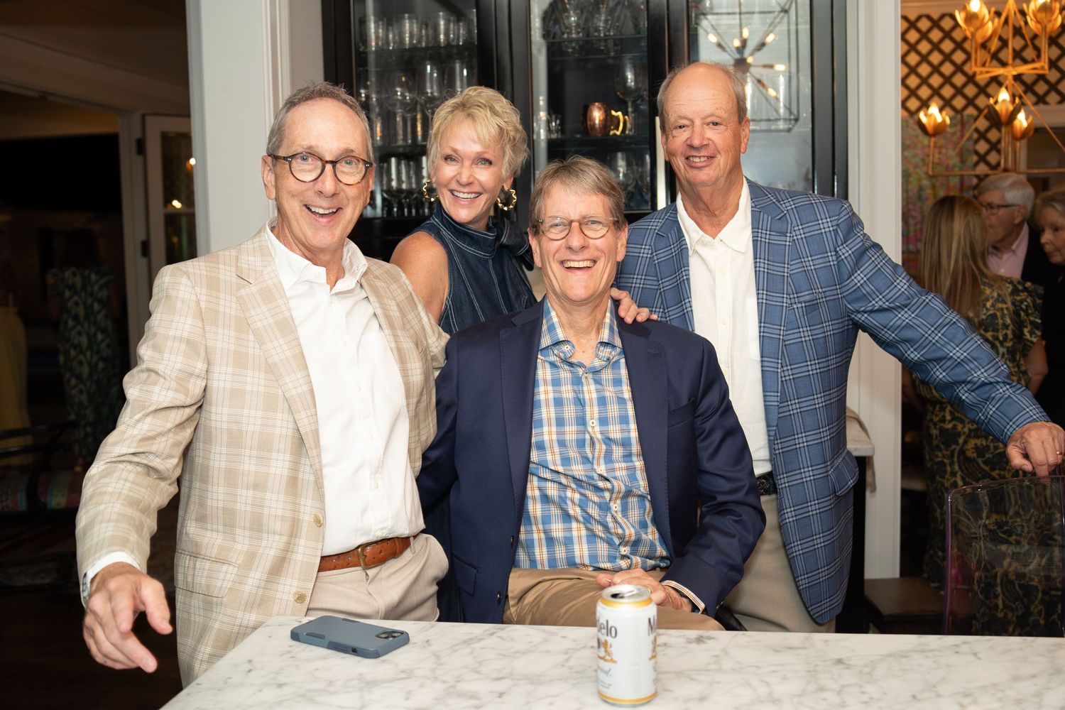 Four smiling adults posing together at an indoor social gathering around a marble table.