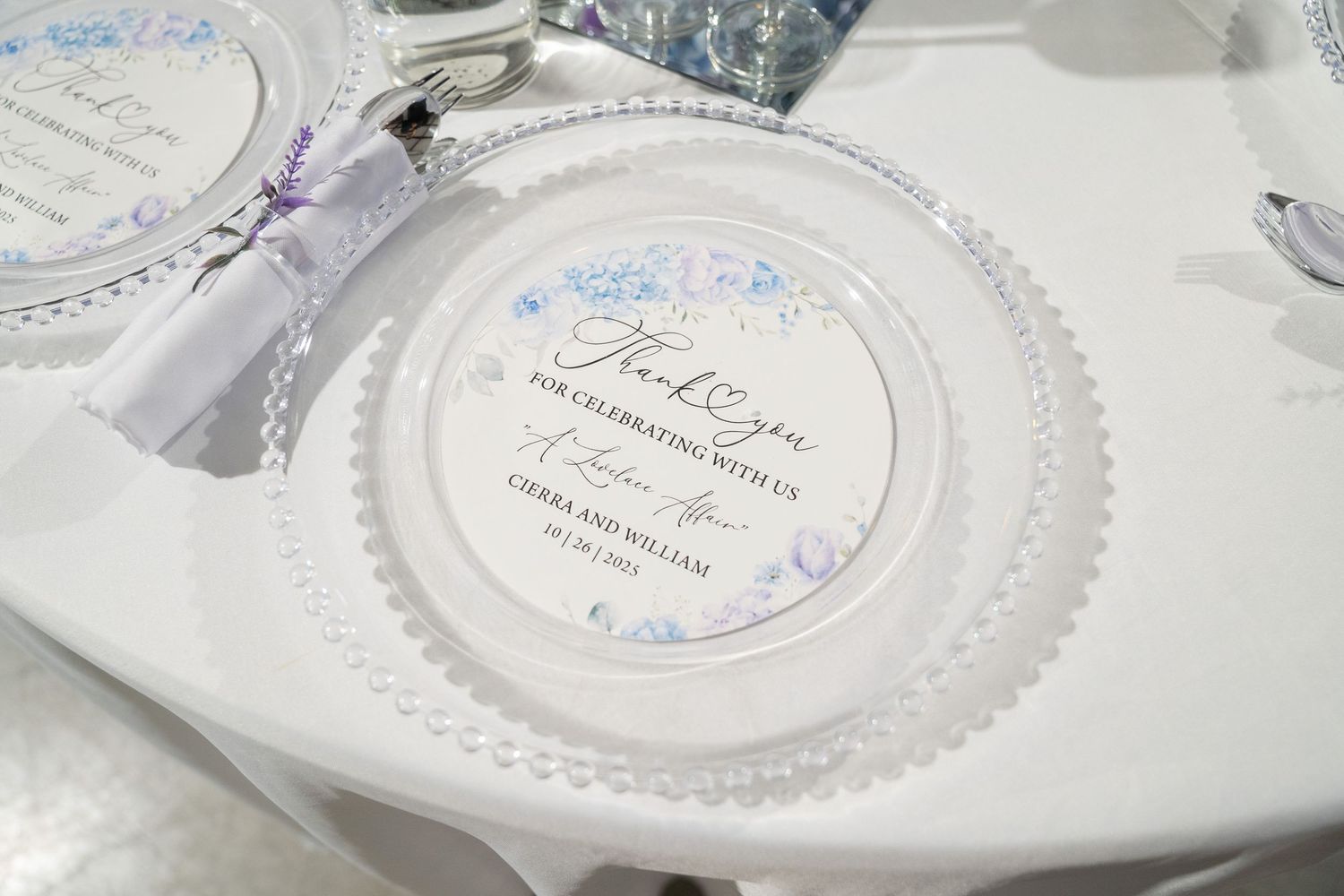 Elegant wedding place setting with personalized thank you charger plate, floral accents, and white linen table decor.
