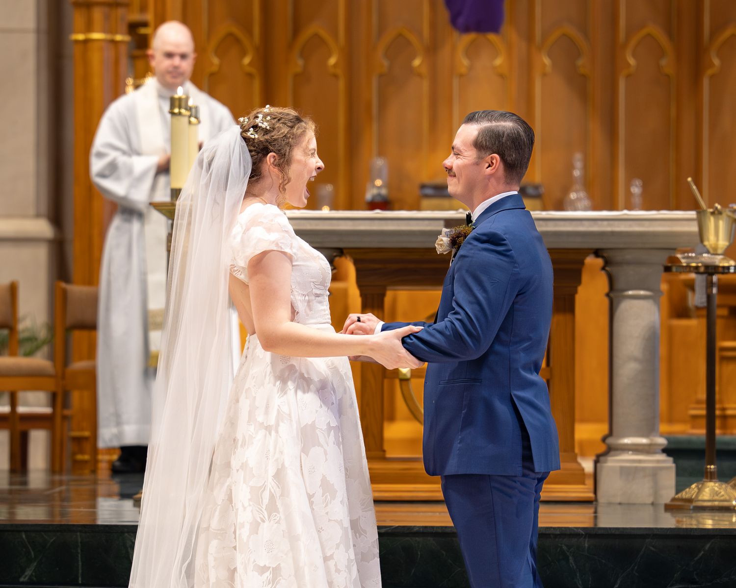 Bride and groom exchange vows at church altar, holding hands in wedding ceremony with officiant standing behind.